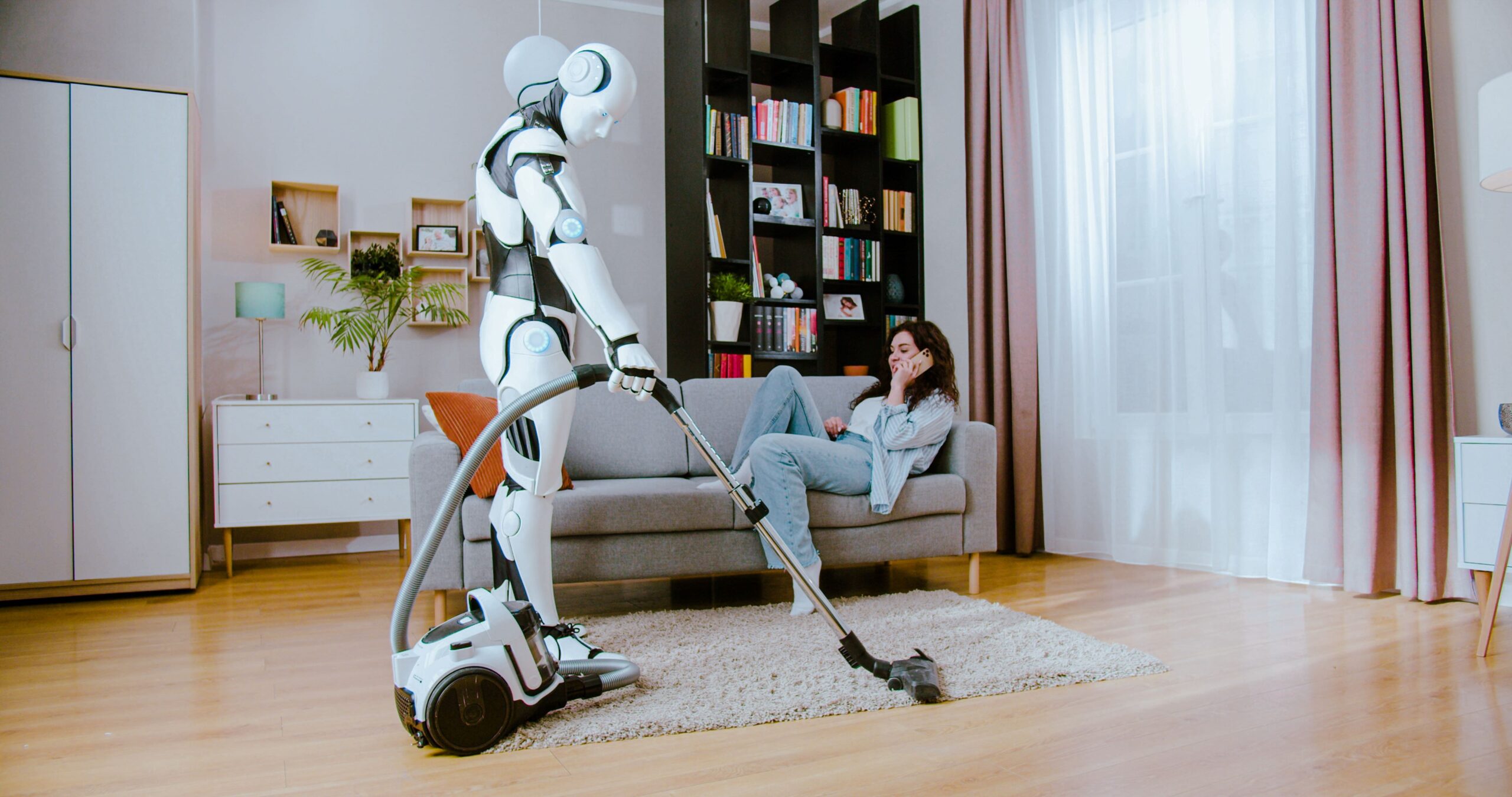 Ein Roboter saugt einen Teppich während eine Person auf einem Sofa sitzt 