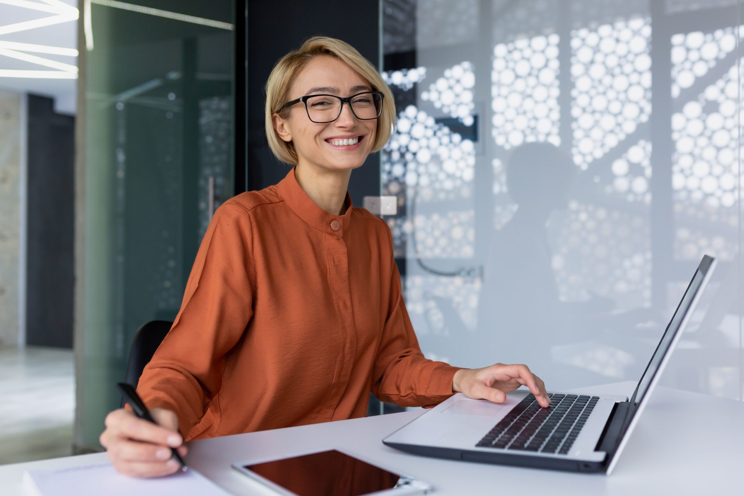 Lachende Frau arbeitet am Laptop mit Notizen – symbolisiert positive Umsetzung von Online Seminarverwaltung im Arbeitsalltag